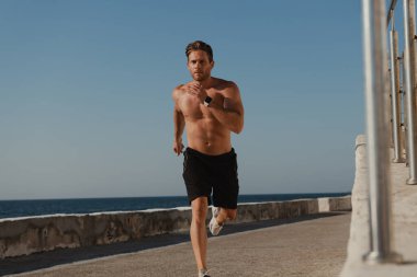 İskelenin orada koşan yakışıklı erkek atlet. Arka planda deniz var.