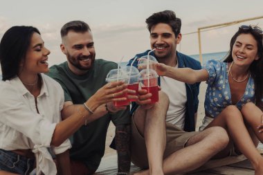 Birlikte sahilde vakit geçirirken kokteyllerle kadeh kaldıran bir grup neşeli genç.