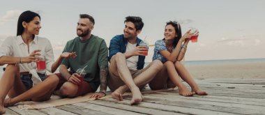 Dört genç arkadaş birlikte sahilde vakit geçirirken yaz kokteyllerinin tadını çıkarıyorlar.