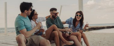 Kumsalda kaygısızca vakit geçirirken soğuk biranın tadını çıkaran dört mutlu genç insan.