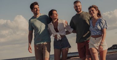 Bir grup neşeli genç arkadaş sahilde yürürken birbirlerine bağlanıyorlar ve gülümsüyorlar.