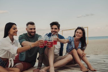 Birlikte sahilde vakit geçirirken kokteyllerle kadeh kaldıran bir grup mutlu genç.