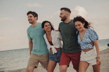 Kumsalda yürürken gülümseyen ve kaynaşan bir grup güzel genç insan.