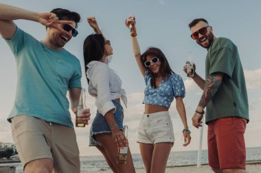 Bir grup neşeli genç, kumsalda dans ederken soğuk biranın tadını çıkarıyorlar.