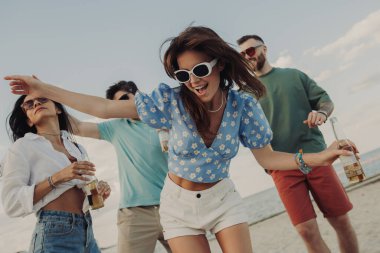 Bir grup güzel genç insan sahilde eğlenirken bira içip dans ediyorlar.