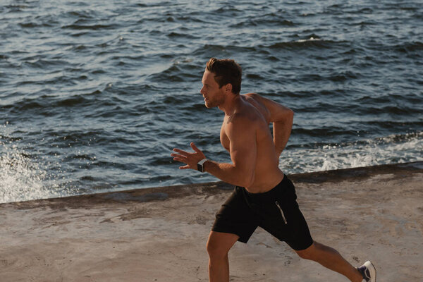 Top view of confident athletic man jogging by the pier with the sea on background