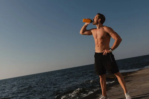 Confident male athlete drinking water while relaxing after sport training seaside