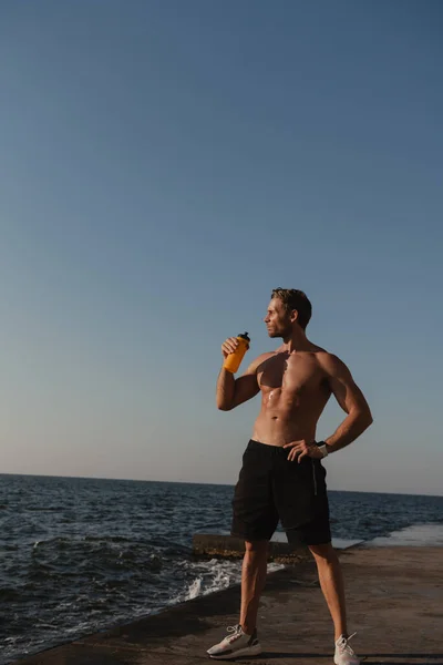 Handsome male athlete drinking water while relaxing after sport training seaside
