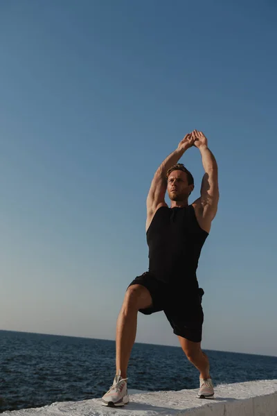 Arkaplanda Deniz Manzaralı Esneme Egzersizleri Yapan Yakışıklı Genç Erkek Sporcu — Stok fotoğraf