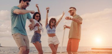 Kumsalda dans ederken soğuk biranın tadını çıkaran dört neşeli genç.