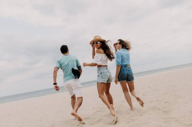 Üç mutlu genç arkadaş sahilde birlikte koşarken kaygısız zaman geçiriyorlar.