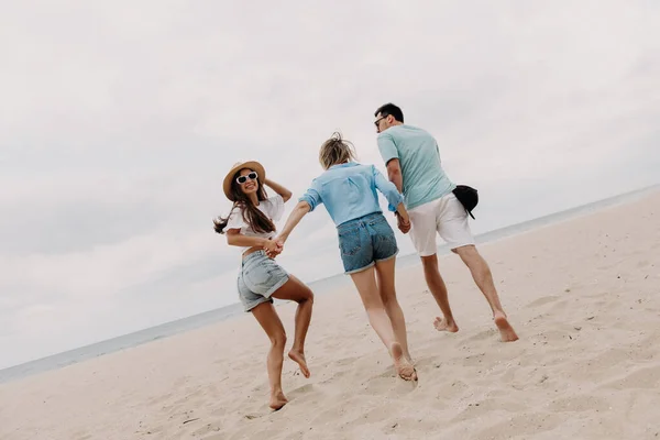 3人の幸せな若い友人が一緒に海にビーチで走っている間楽しい時間を過ごします — ストック写真