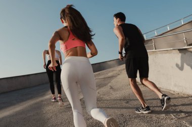 Spor giyim kuşamında birlikte koşan üç gencin arka görüntüsü.