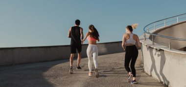 Spor giyim kuşamında birlikte koşan üç gencin arka görüntüsü.