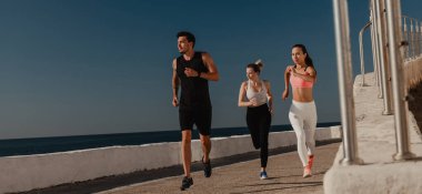 Spor giyim sektöründe bir sürü genç, birlikte deniz kenarında koşarken konsantre görünüyorlar.