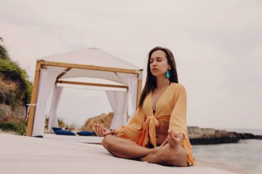 Boho 'da çekici genç bir kadın. Nilüfer pozisyonu almış, deniz kenarında meditasyon yapıyor.