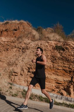 Açık havada antrenman yaparken dağa karşı koşan kendine güvenen erkek sporcu.