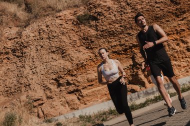 Spor kıyafetlerinde, açık havada antrenman yaparken dağa karşı koşan kendine güvenen genç bir çift.