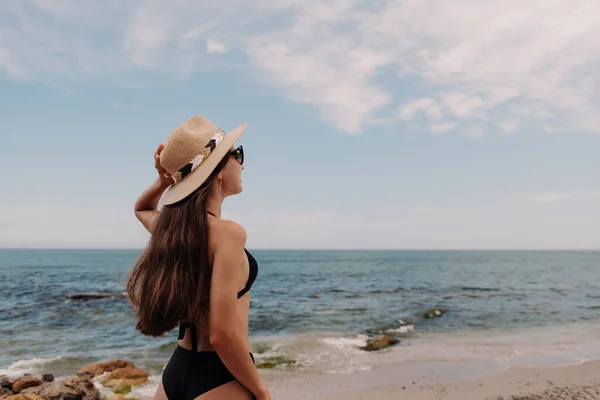 ビーチで海を眺めながら帽子を調整する水着の魅力的な女性のリアビュー — ストック写真