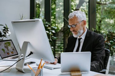 Modern ofiste çalışırken bilgisayar kullanan konsantre bir iş adamı.