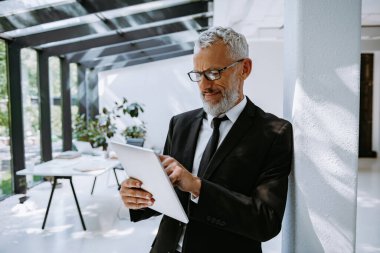 Ofiste dikilirken dijital tablet kullanan kendinden emin bir iş adamı.