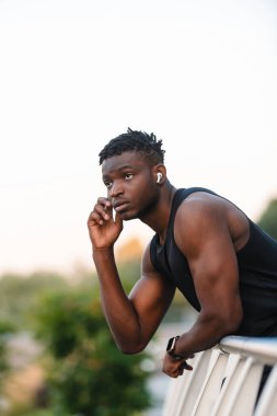 Spor kıyafetli yakışıklı Afrikalı adam dışarıda antrenman yaptıktan sonra kulaklıklarını ayarlıyor.