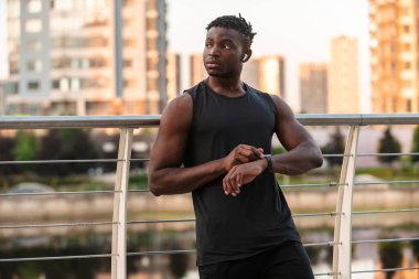 Spor giyim sektöründe yakışıklı Afrikalı bir adam dışarıda antrenman yaparken akıllı saat kullanıyor.
