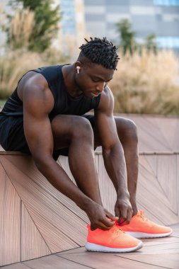 Spor kıyafetleri içinde kendine güvenen Afrikalı bir adam spor antrenmanlarına hazırlanırken ayakkabı bağcıklarını bağlıyor.