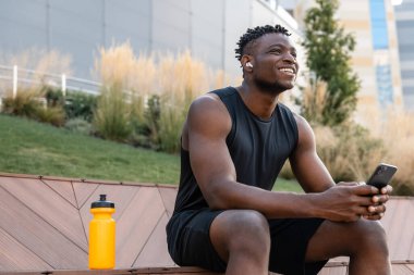 Spor giyim sektöründe yakışıklı Afrikalı adam akıllı telefon kullanıyor ve antrenmandan sonra gülümsüyor.