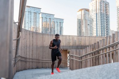Spor kıyafetli yakışıklı Afrikalı adam merdivenlerden yukarı çıkarken konsantre olmuş görünüyor.