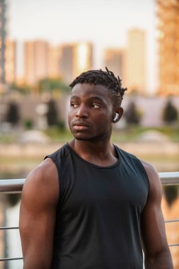 Spor giyim ve kulaklık giyen kendine güvenen Afrikalı adam dışarıda antrenman yaparken mola veriyor.