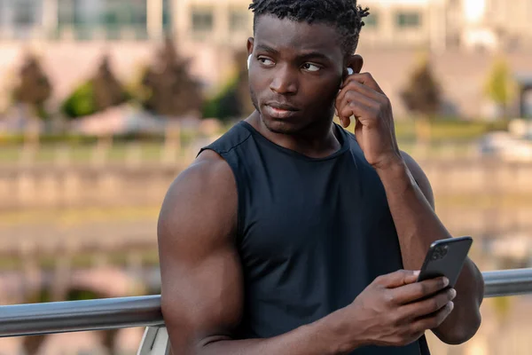 Confident African man in sportswear using smart phone while resting after training outdoors