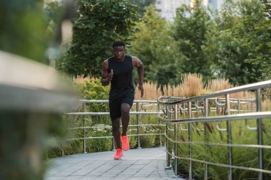 Spor kıyafetleri içinde yakışıklı Afrikalı bir adam. Dışarıda koşarken konsantre görünüyor.