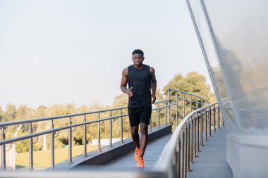 Spor giyim sektöründe tam boy Afrikalı sporcu açık havada koşarken konsantre görünüyor.