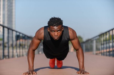 Spor giyimli kendine güvenen genç Afrikalı sporcu dışarıda egzersiz yaparken şınav çekiyor.