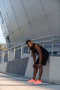 Spor kıyafetleri içinde yorgun Afrikalı bir adam antrenmandan sonra dizlerinin üstüne çöküp dinleniyor.