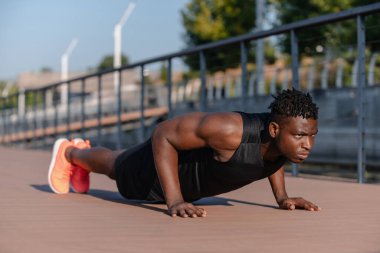 Spor kıyafetli kendine güvenen Afrikalı adam dışarıda egzersiz yaparken şınav çekiyor.