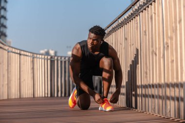Spor giyimli kendinden emin Afrikalı sporcu sabah koşusuna hazırlanırken ayakkabı bağcıklarını bağlıyor.