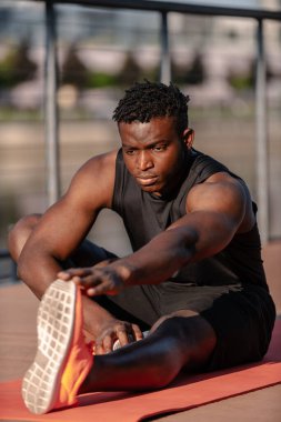 Spor giyimli kendinden emin genç Afrikalı adam dışarıda esneme egzersizleri yapıyor.