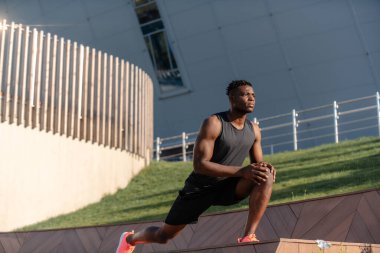 Spor giyim kuşağında kendine güvenen genç Afrikalı adam dışarıda antrenman yaparken esneme egzersizleri yapıyor.