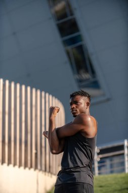 Spor kıyafetleri içinde konsantre olmuş genç Afrikalı adam dışarıda antrenman yaparken esneme egzersizleri yapıyor.