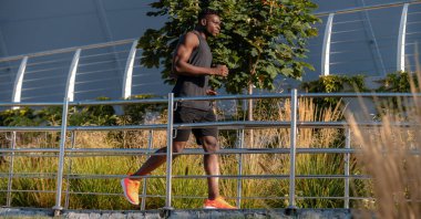 Spor giyimli kendinden emin Afrikalı atlet açık havada koşarken konsantre görünüyor.