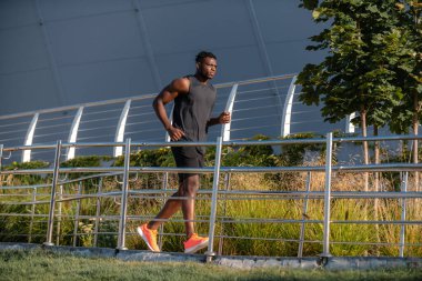 Spor giyim sektöründe tam boy Afrikalı adam açık havada koşarken konsantre görünüyor.
