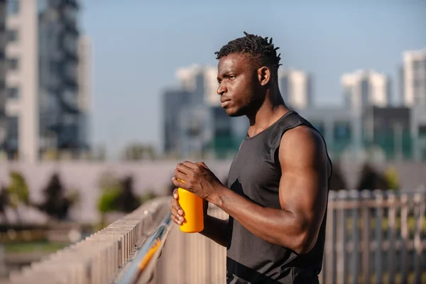 Confident African man in sportswear holding water bottle while resting after training outdoors