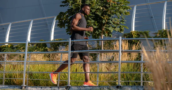 Spor giyimli kendinden emin Afrikalı atlet açık havada koşarken konsantre görünüyor.