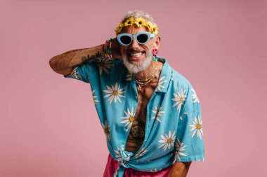 Pembe arka planda gülümseyen şık gömlekli ve çiçekli bir çelenk takmış olgun bir gay.