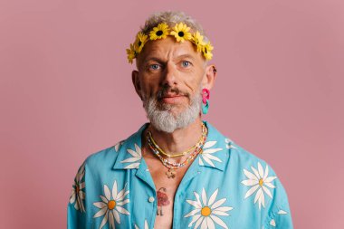 Pembe arka planda duran şık gömlekli ve çiçekli yakışıklı bir adam.