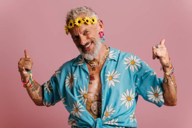 Pembe arka planda duran şık gömlekli havalı bir adam ve başında çiçek çelengi.