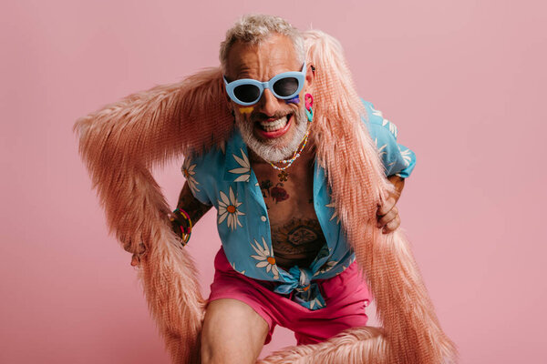 Happy mature gay man with rainbow flag make-up looking out of the picture frame on pink background