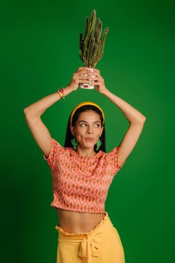 Kafasında kaktüs tutan ve yeşil arka planda gülümseyen mutlu genç kadın.